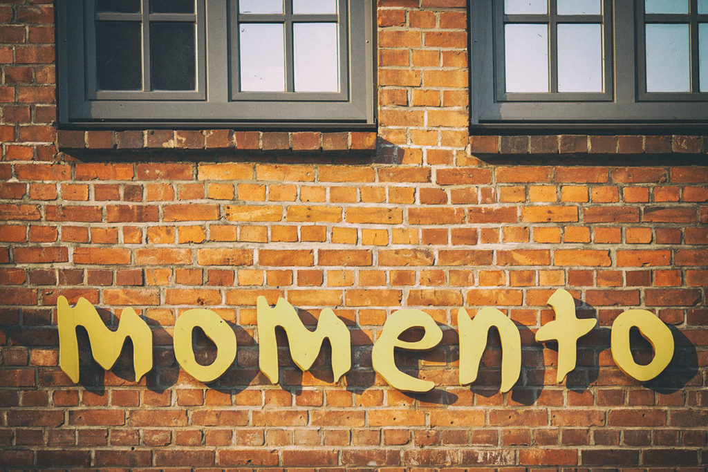 Backstein-Häuserwand mit Kassettenfenstern und der Aufschrift "momento"